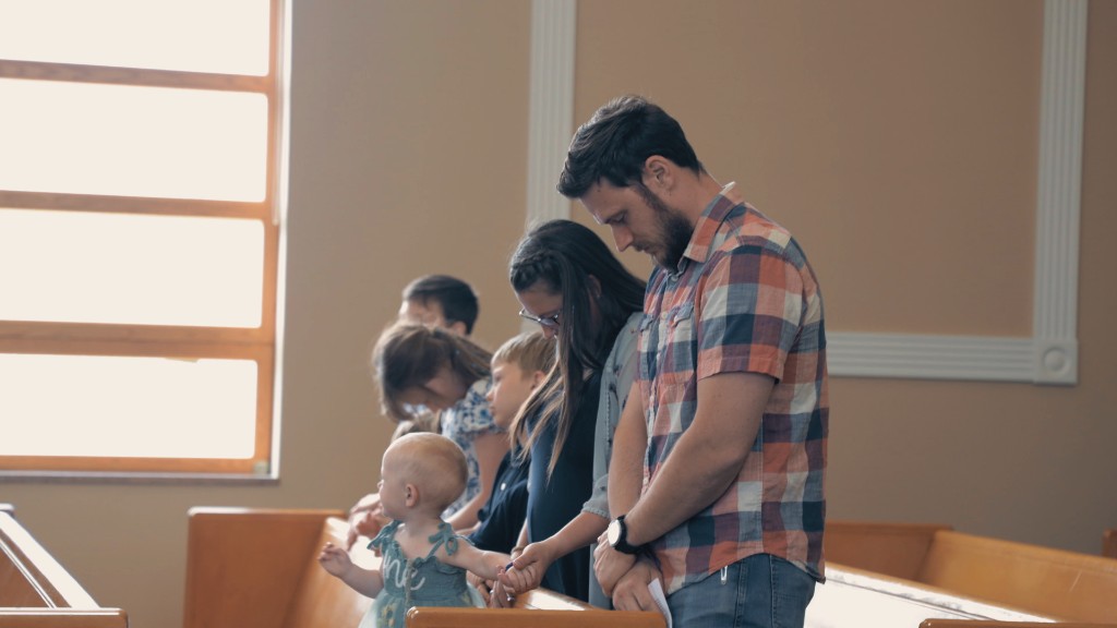 A family standing together in the pew, holding hands during prayer