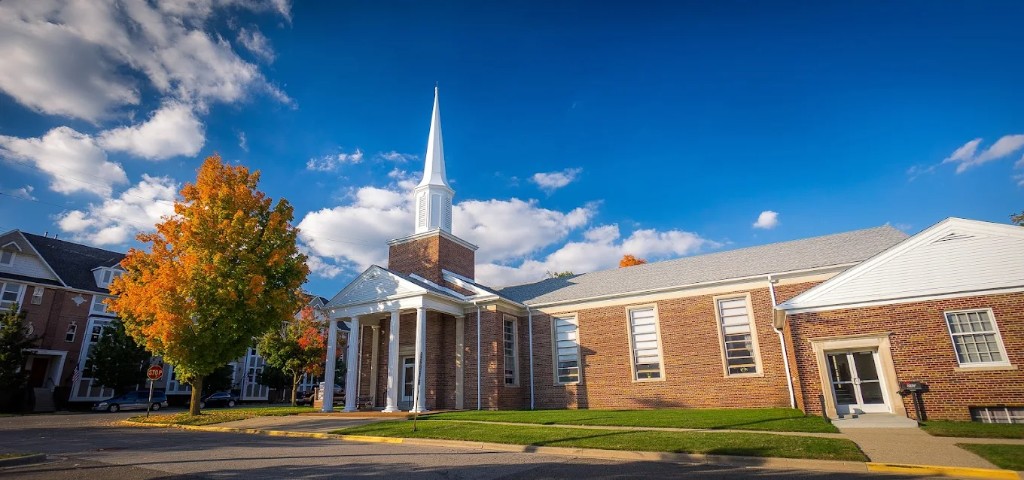 Christ Church Livingston County: red brick exterior with white columns, steeple, and autumn trees in Howell, Michigan